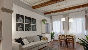 A living room with a sofa, dining table, chairs, and artwork on the wall. - Mamo Florence - Ghibellina Apartment (Florence)