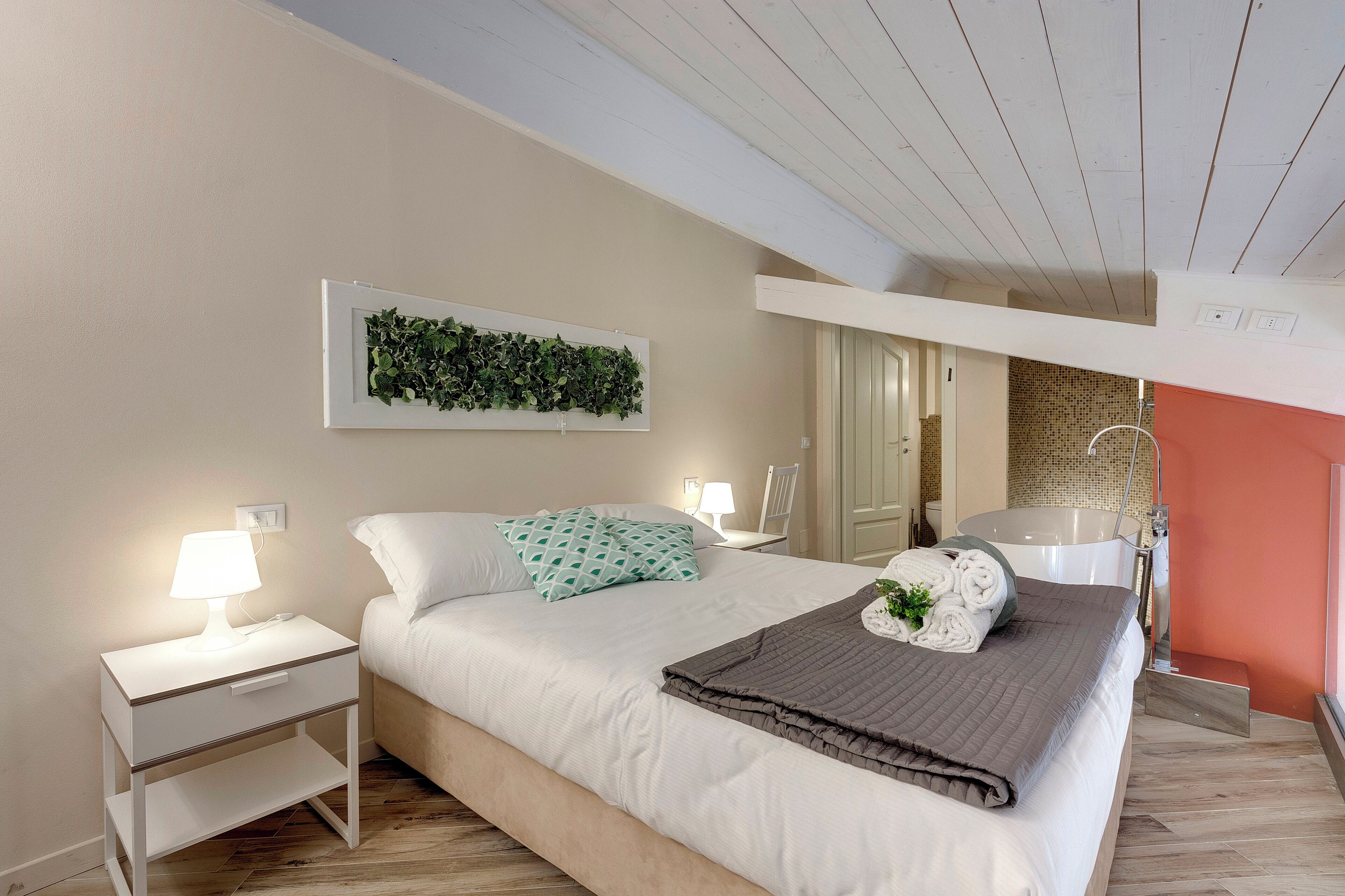 Ein Schlafzimmer mit Bett, Nachttischen, einem an der Wand befestigten Kunstwerk, einem Badezimmer mit Badewanne und einem gefliesten Boden.