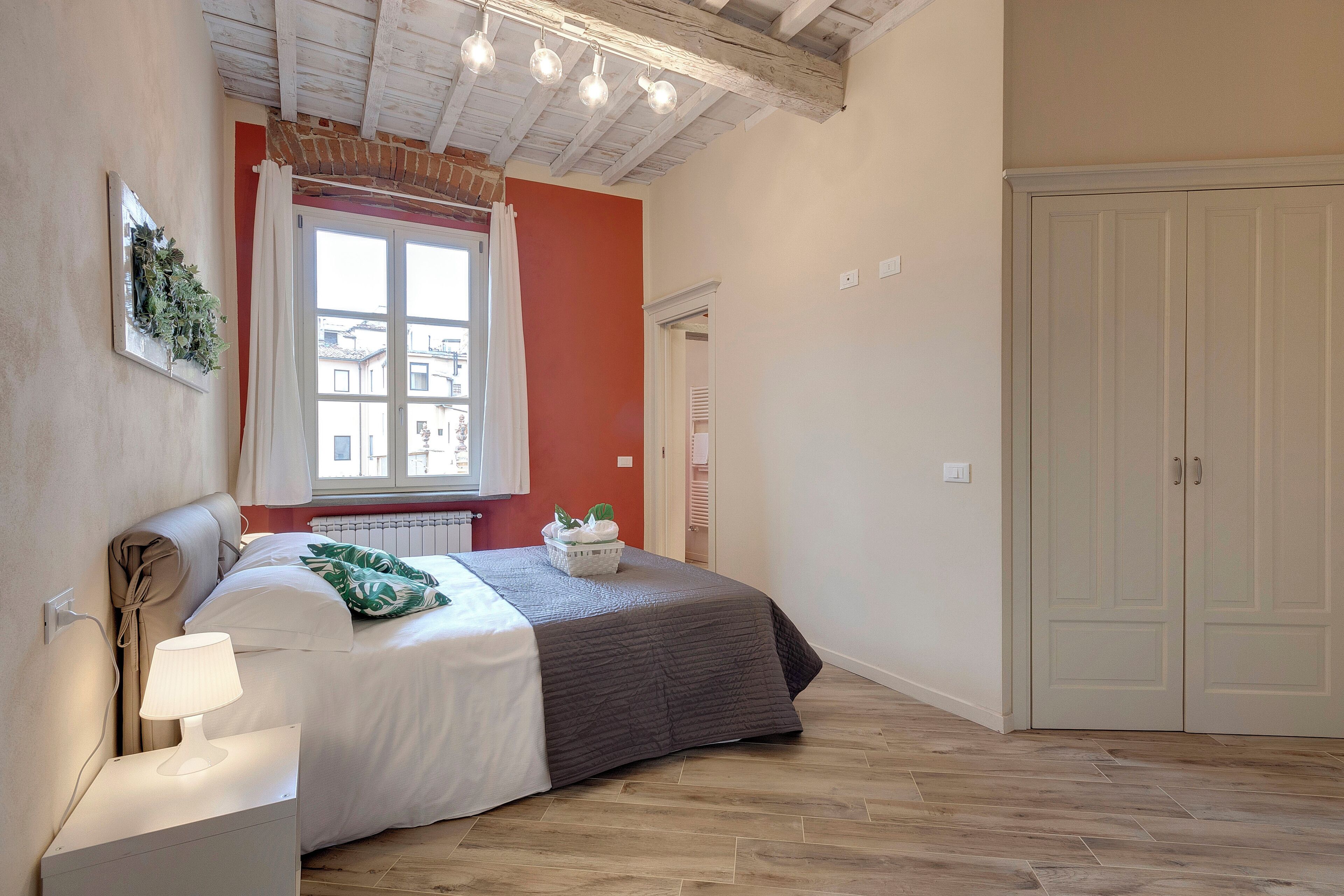 A bedroom with a bed, bedside lamp, window with curtains, and a wardrobe.