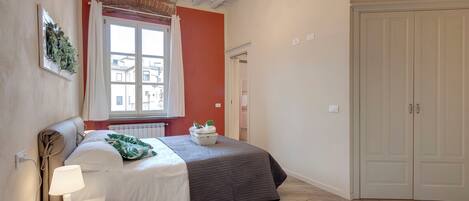 A bedroom with a bed, bedside lamp, window with curtains, and a wardrobe.