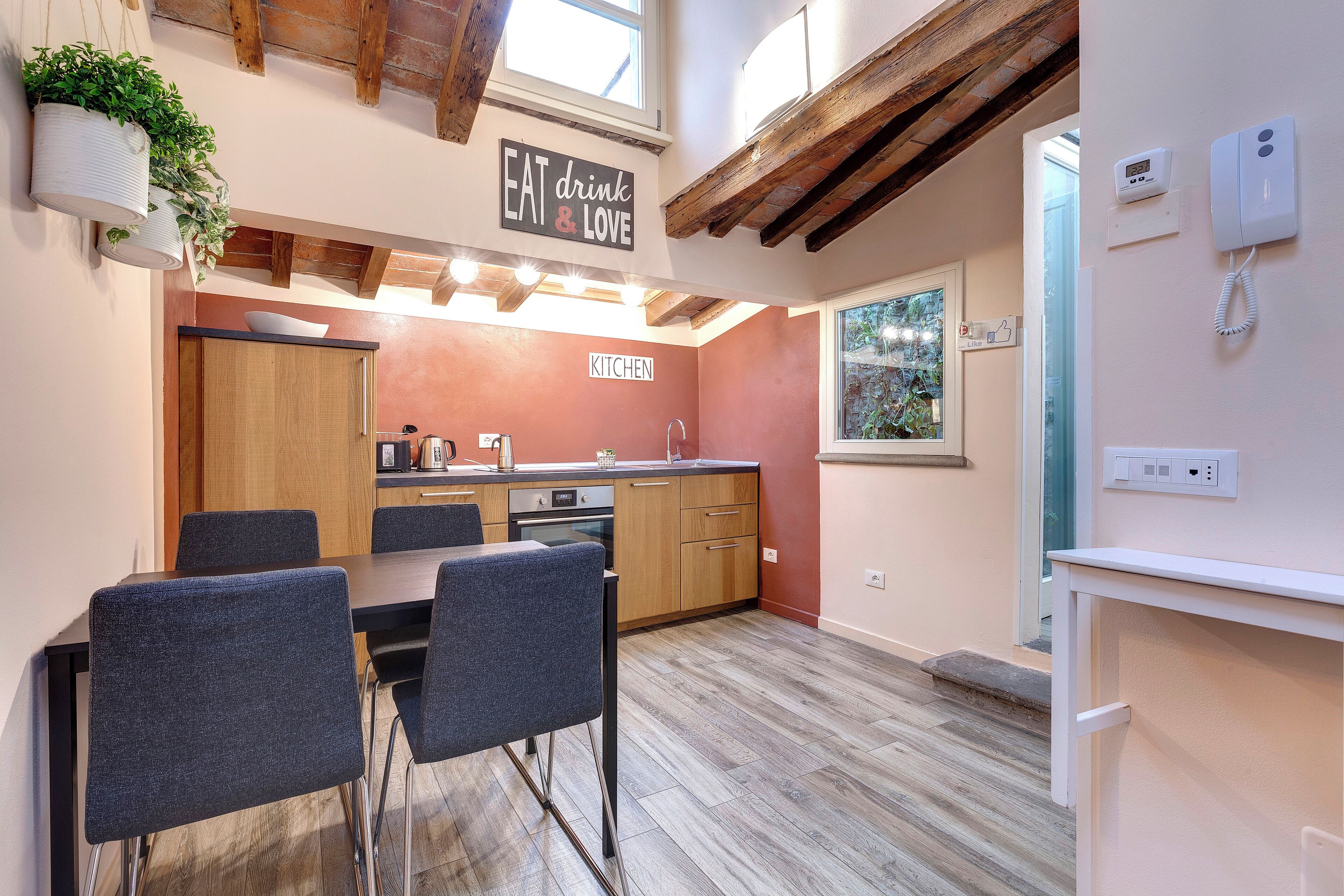 A modern kitchen with wooden cabinets, a dining area with grey chairs, and a sign that says "EAT drink & LOVE".