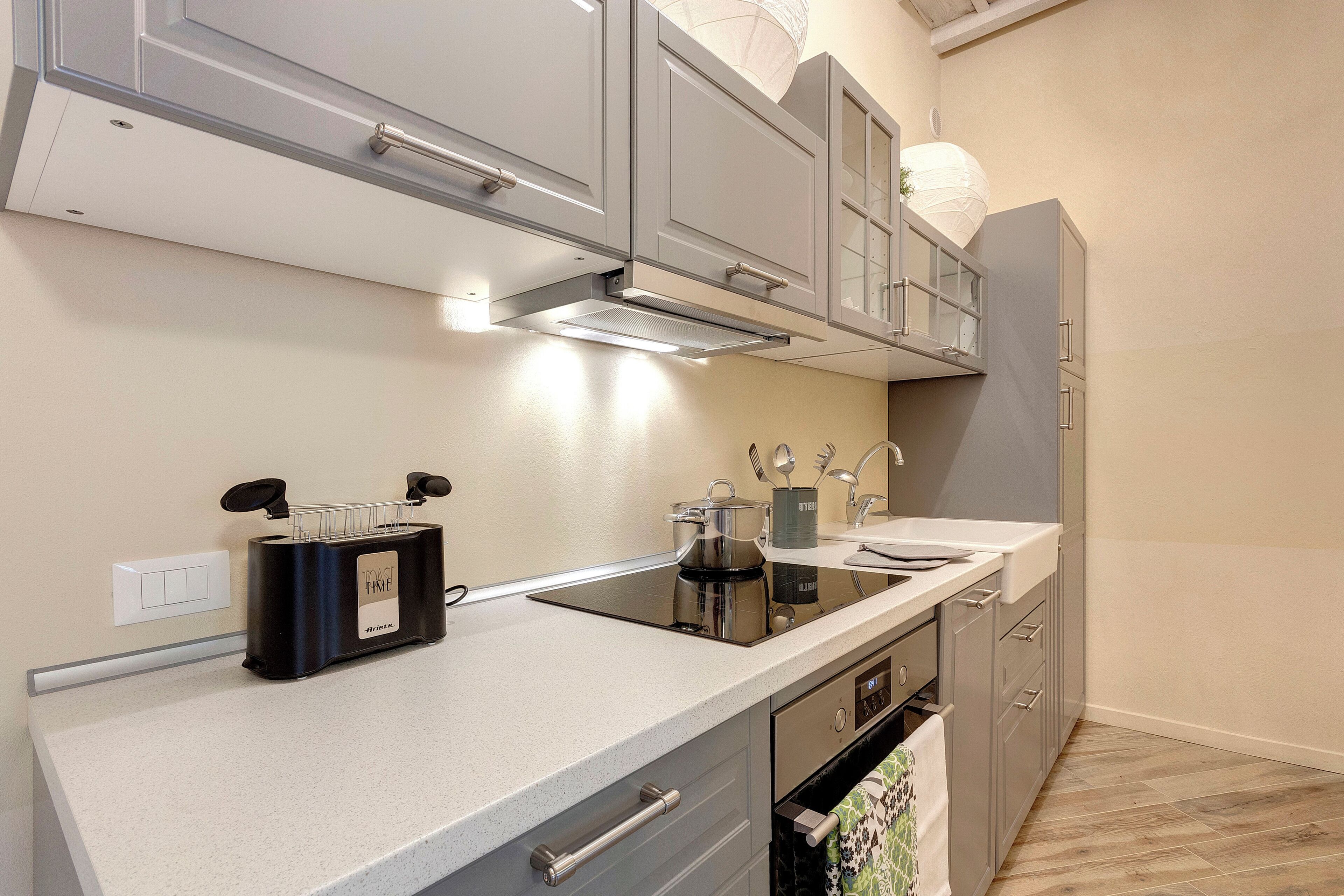 Una cocina moderna con armarios grises, una placa de inducción negra y un horno de acero inoxidable.