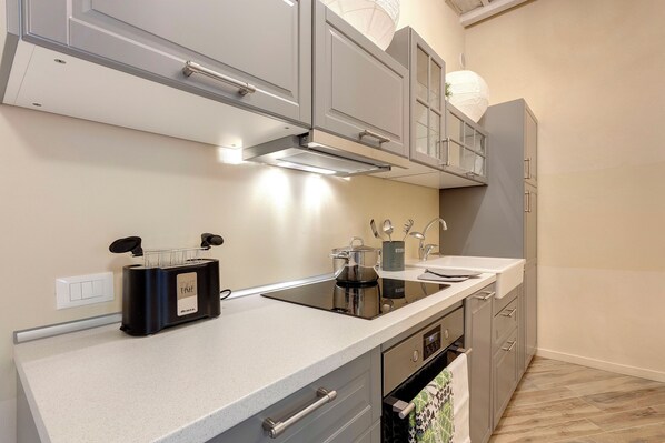 A modern kitchen with grey cabinets, a black induction cooktop, and a stainless steel oven. - Vertical Garden Apartments by Mamo Florence (Florence)