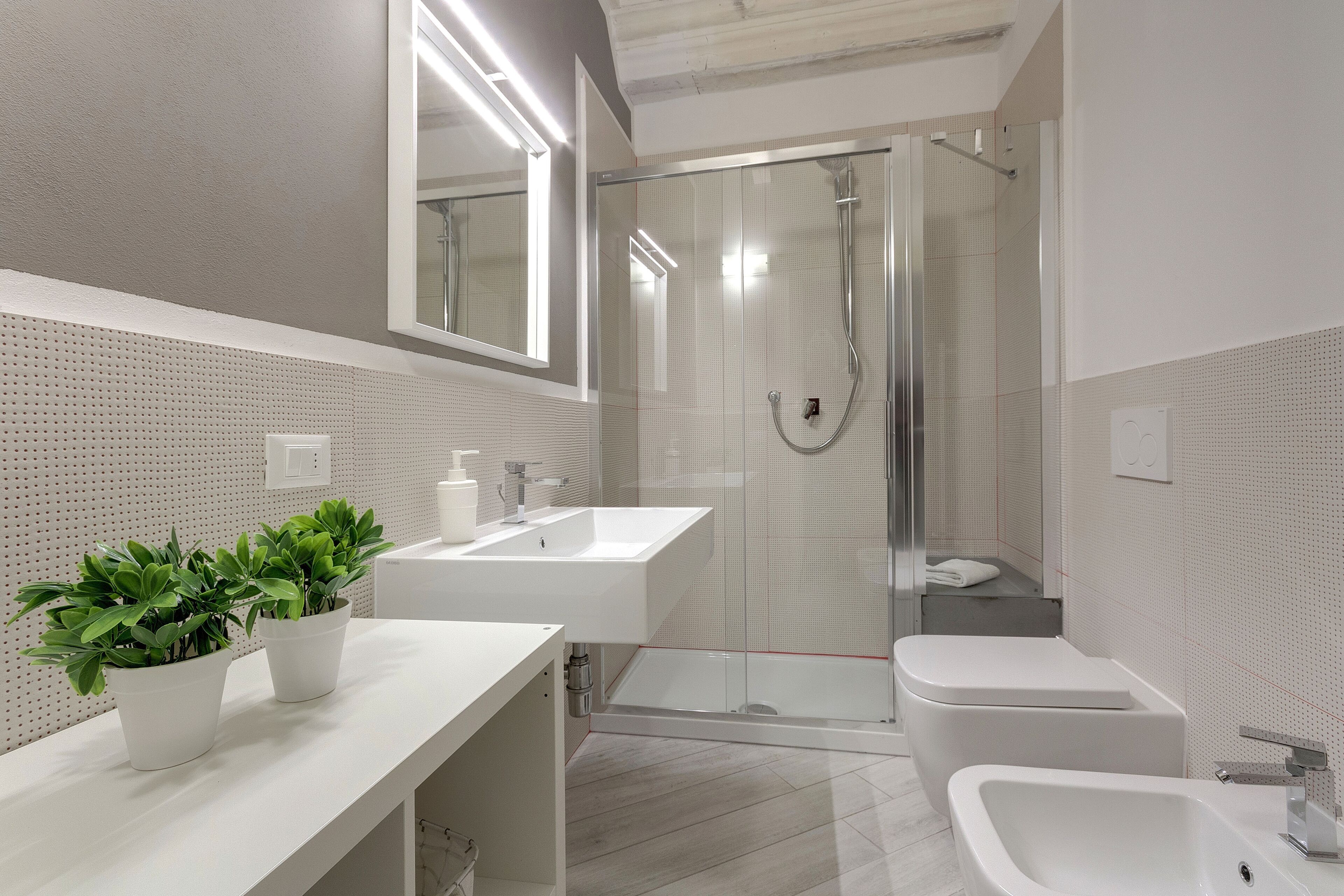 A modern bathroom with two sinks, a shower, and a bidet.