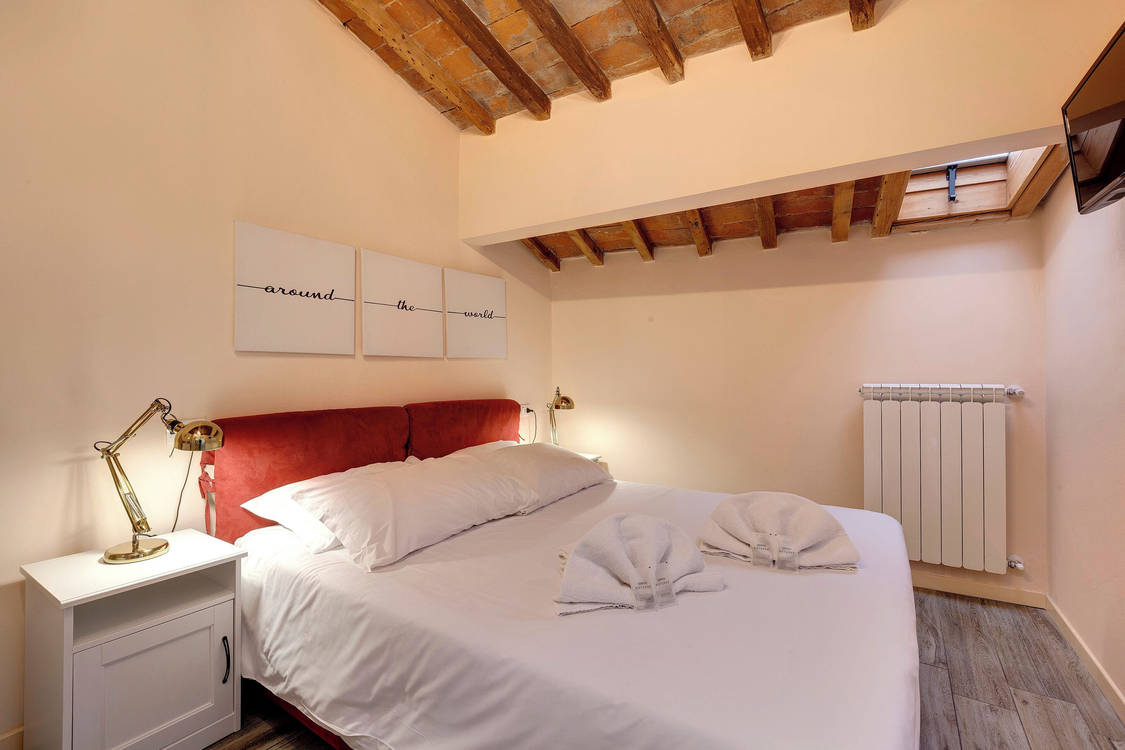 A bedroom with a bed, bedside table, lamp, and artwork on the wall.