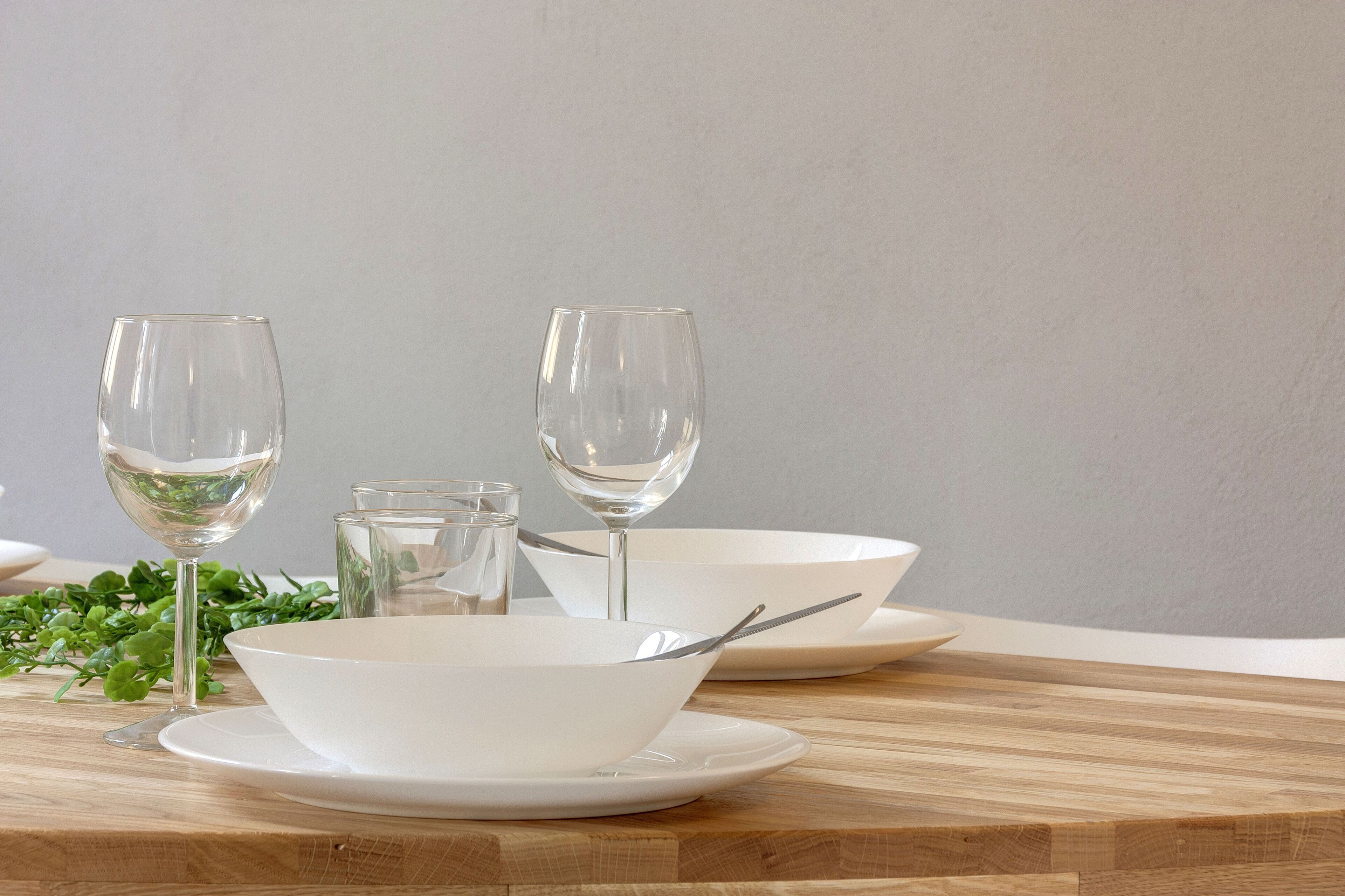 Une table à manger avec de l’assiette blanche, des bols et des verres à vin.