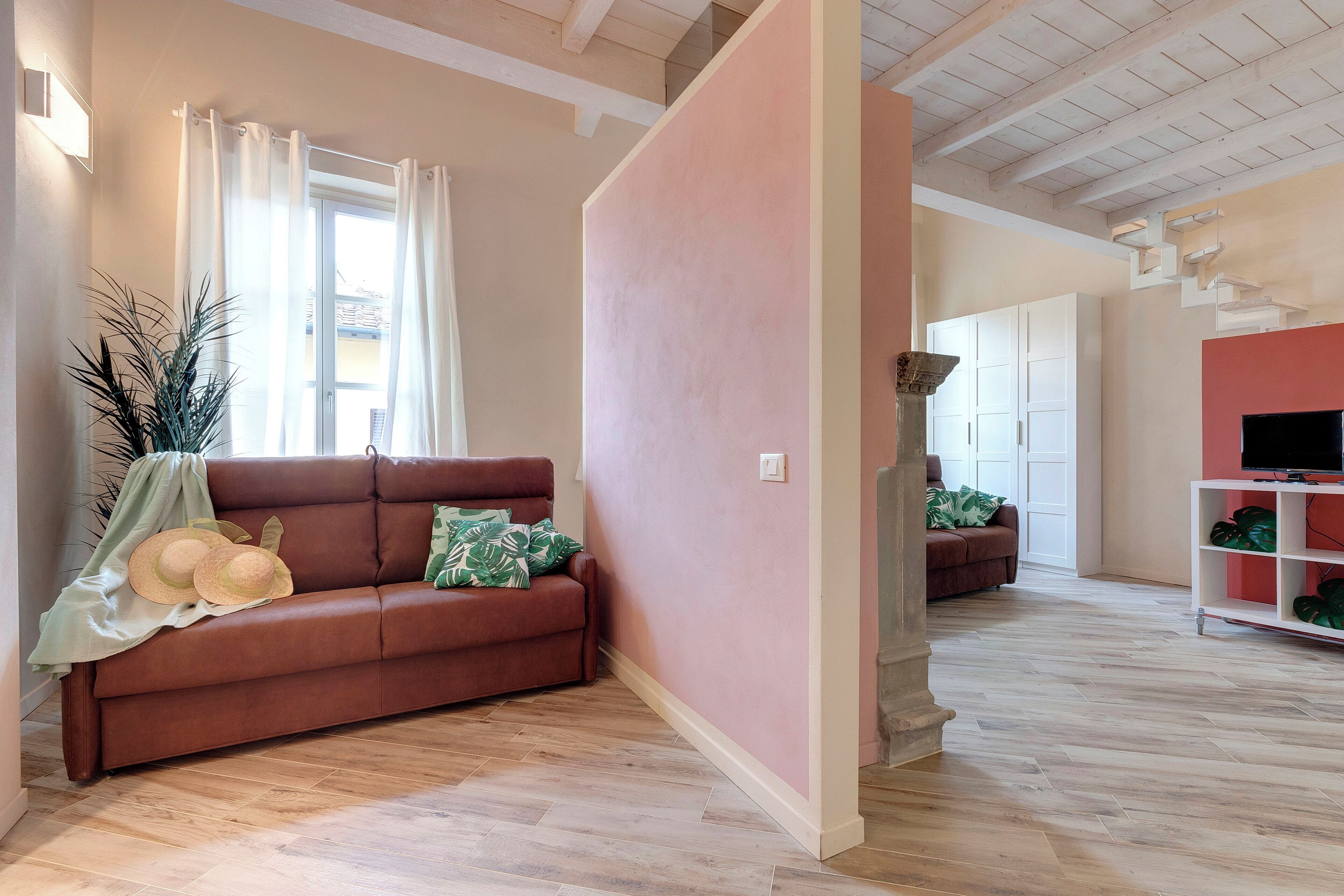 A living room with a brown sofa, a white TV stand, and a pink accent wall.