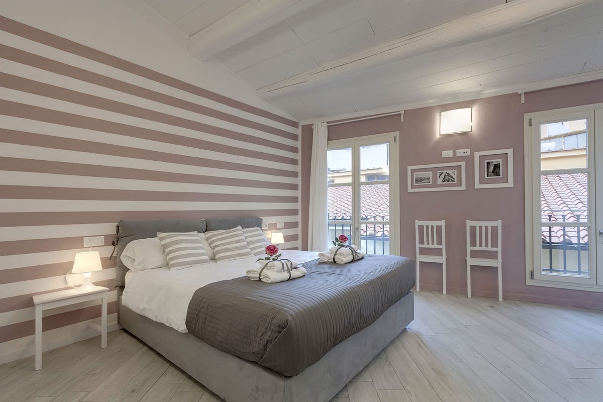 A bedroom with a bed, bedside tables, a window, and a balcony view.