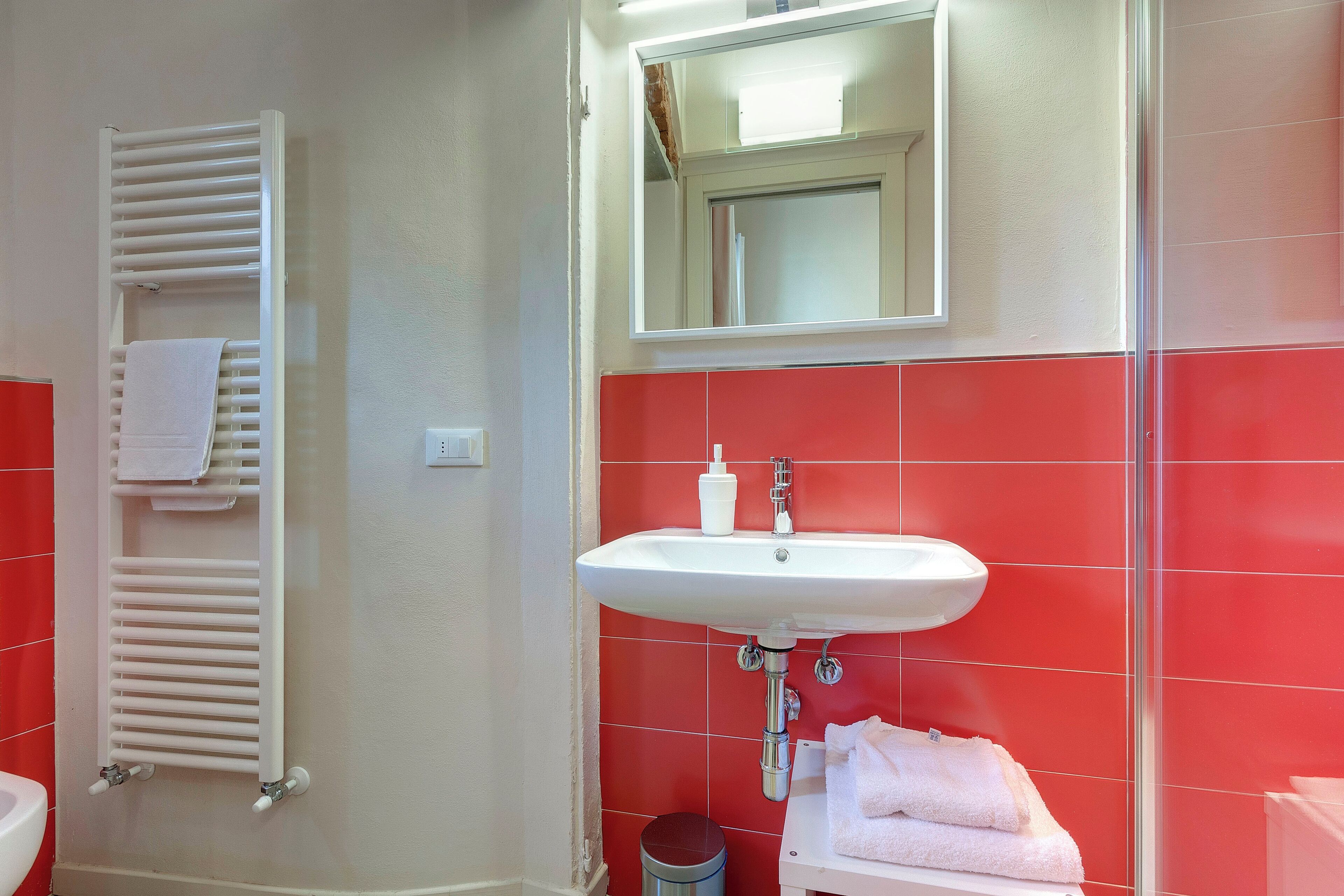 Un bagno con lavandino bianco, piastrelle rosse, un portasciuga e uno specchio.