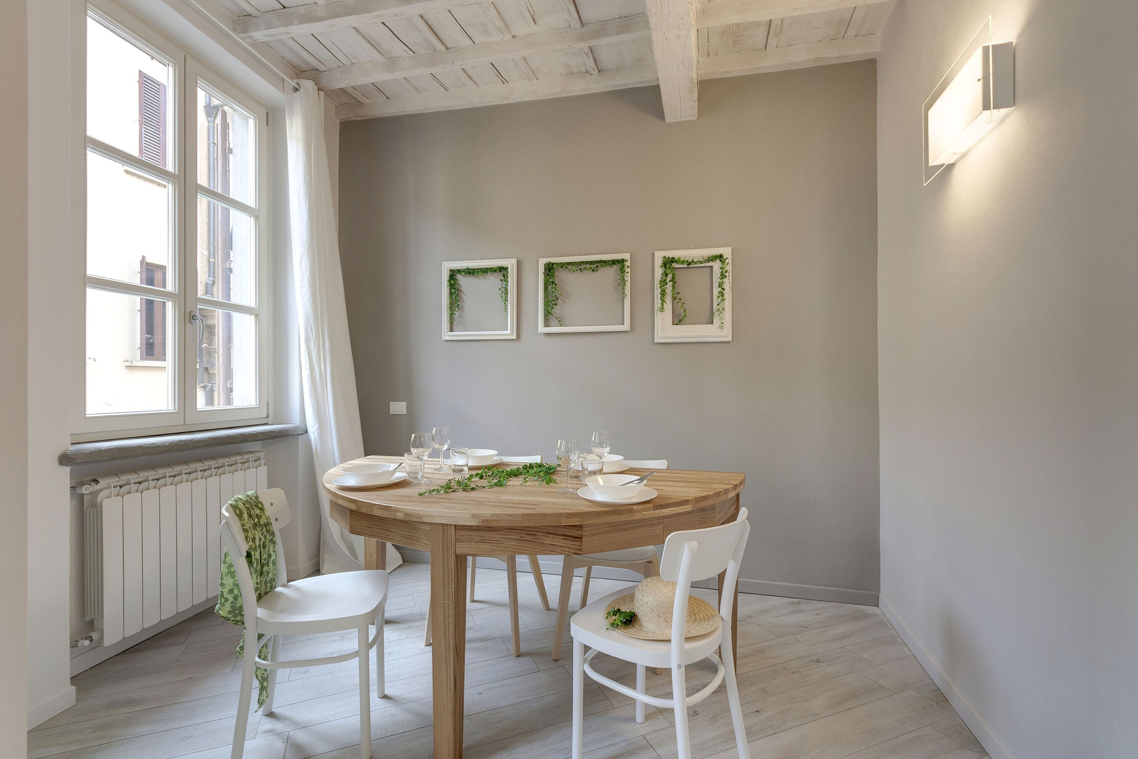A dining area with a round wooden table, white chairs, and a window with curtains.