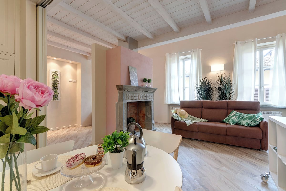 A cozy living room with a fireplace, a brown sofa, and a dining table with pastries and a teapot.