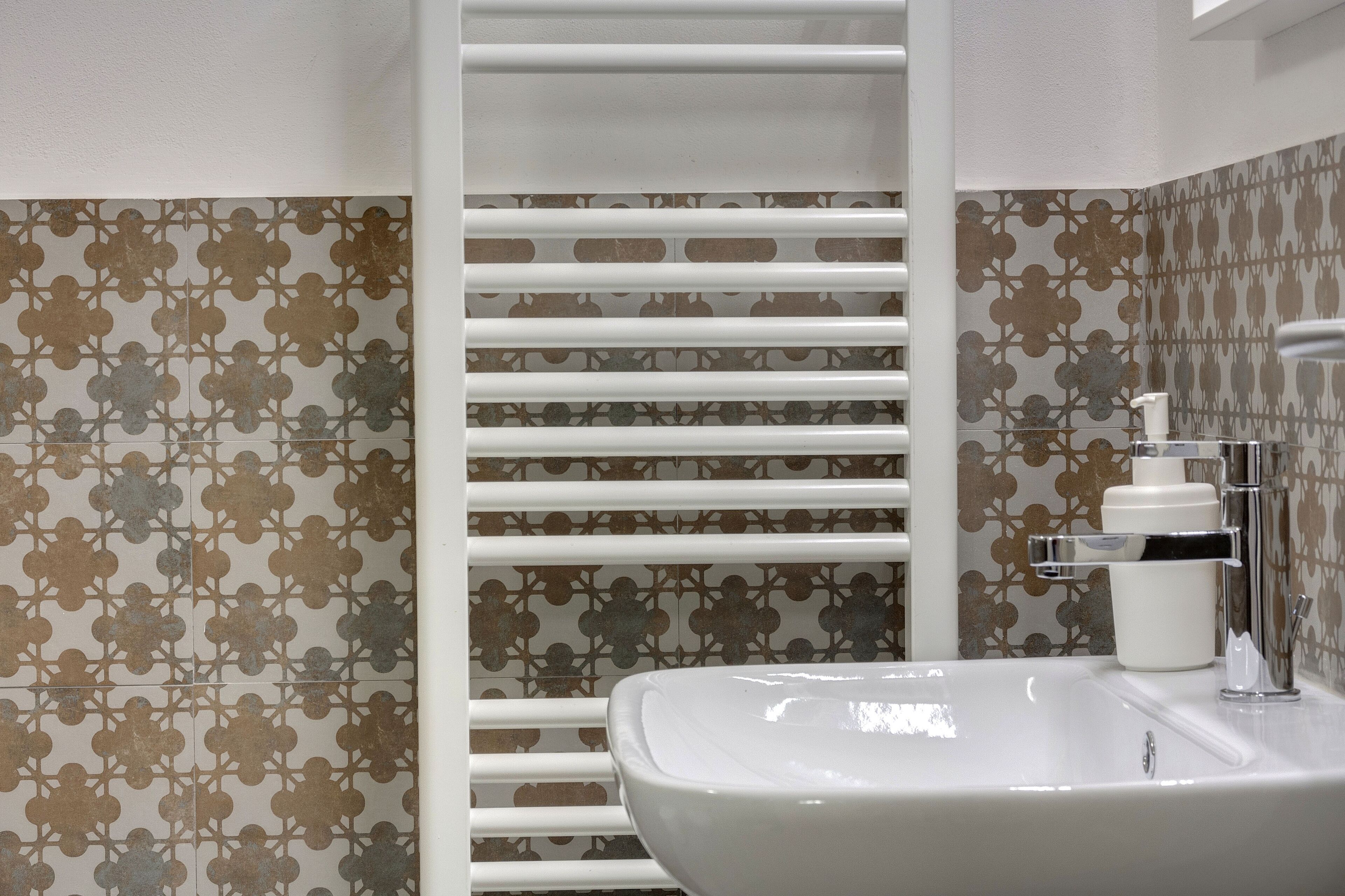 A bathroom with a white sink, a towel rack, and patterned tiles.
