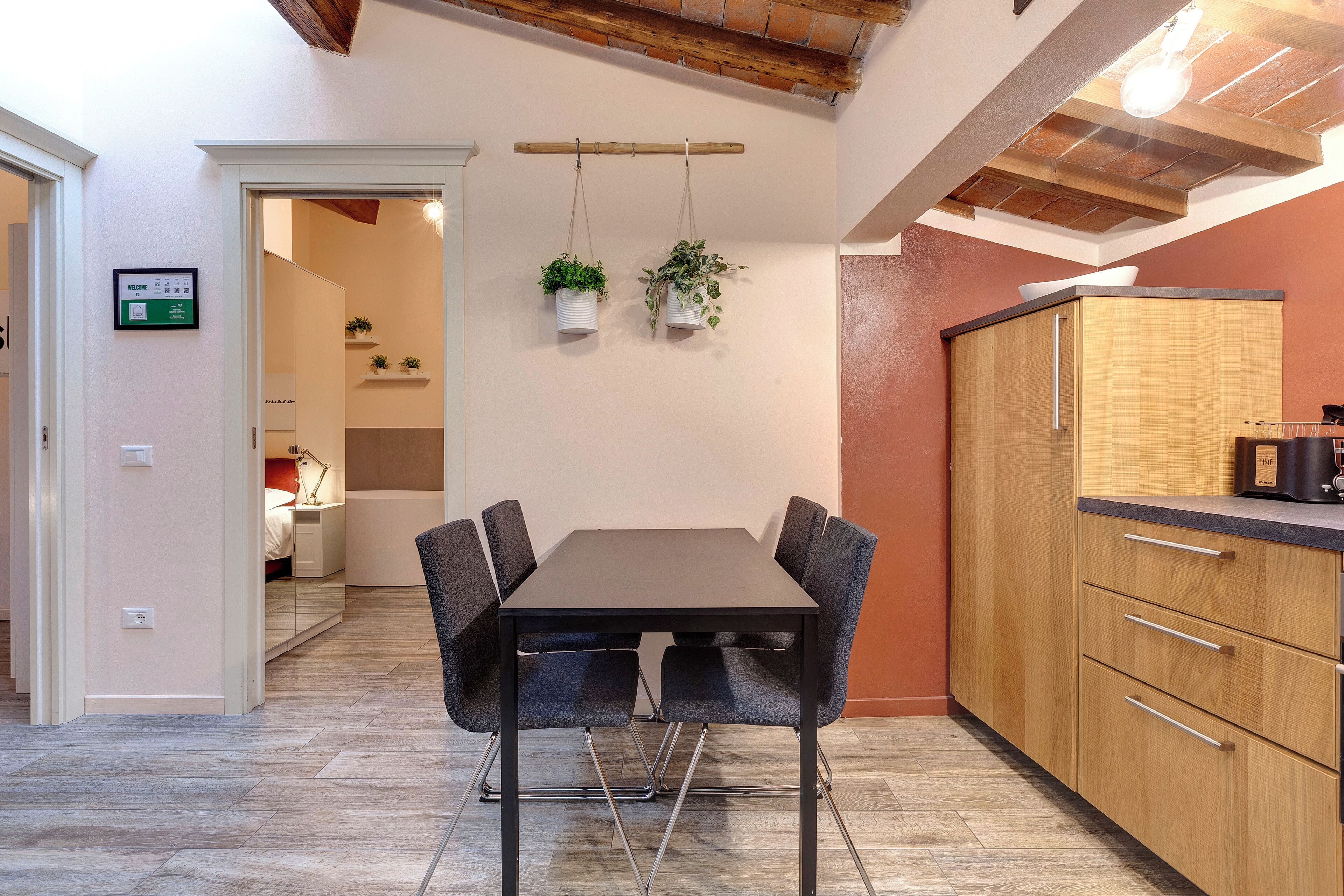 Een moderne keuken met een houten kast, een zwarte eettafel met stoelen en hangende planten.