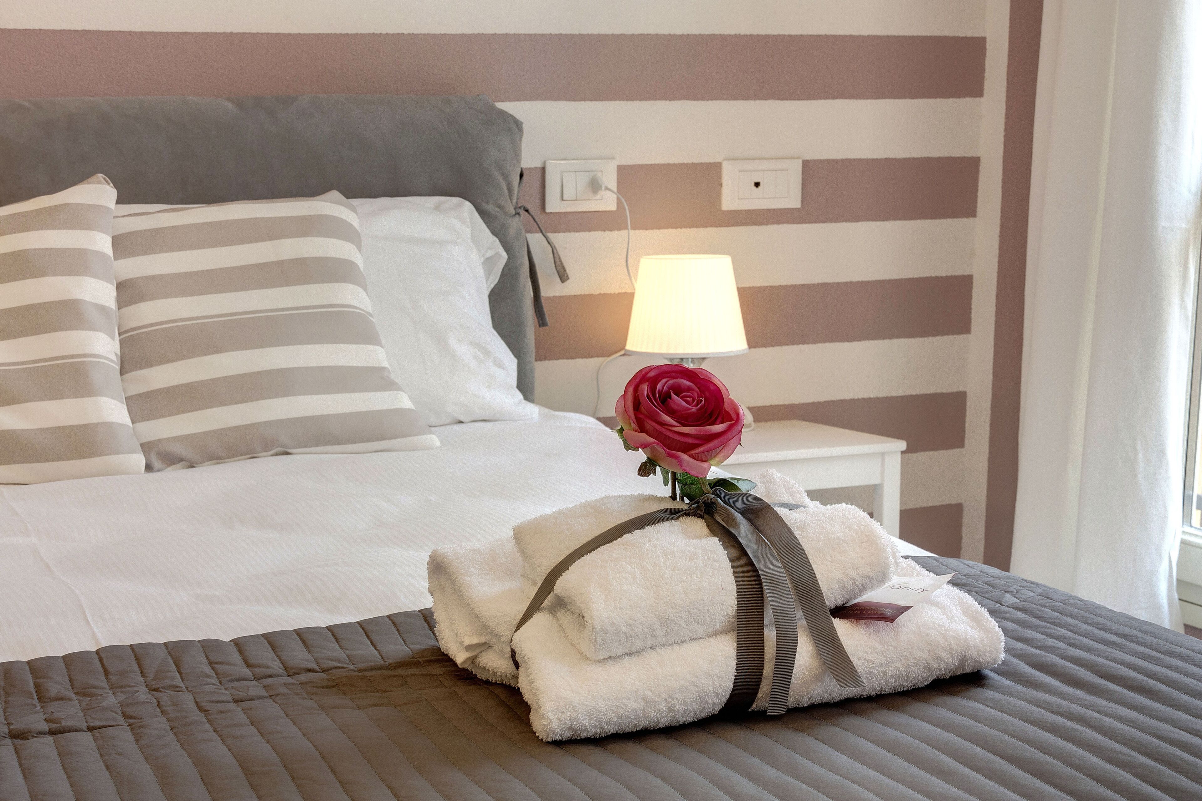 A neatly made bed with striped pillows, a rose, and folded towels on a bed with a striped headboard.