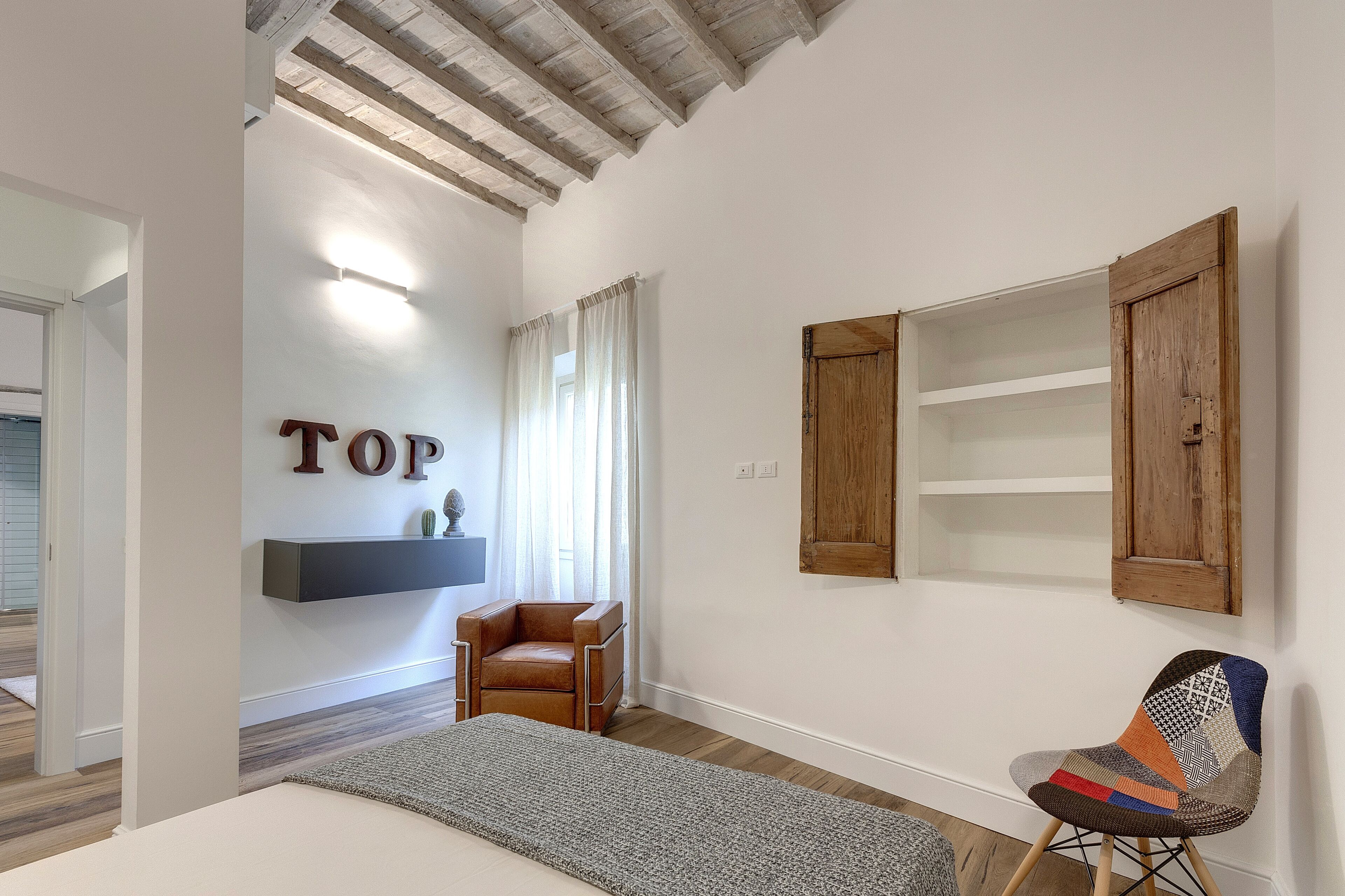 Een kamer met een bed, een stoel, een plank met een plant, een houten kast en een muur met de tekst 'TOP'.