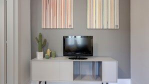A modern living room with a flat-screen TV on a white console, two striped artworks above, and a cactus plant on the console. - Mamo Florence - Il Moro Apartment (Florence)