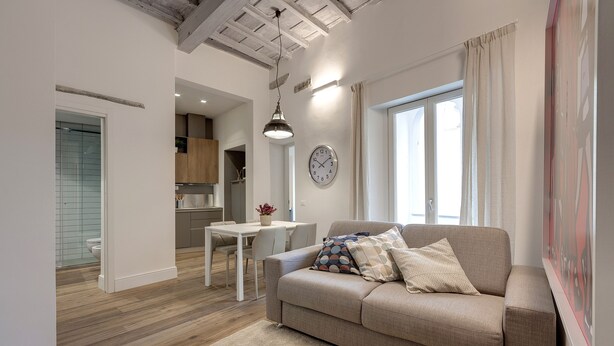 A modern living room with a beige sofa, a dining table, and a kitchen in the background. - Mamo Florence - Il Moro Apartment (Florence)