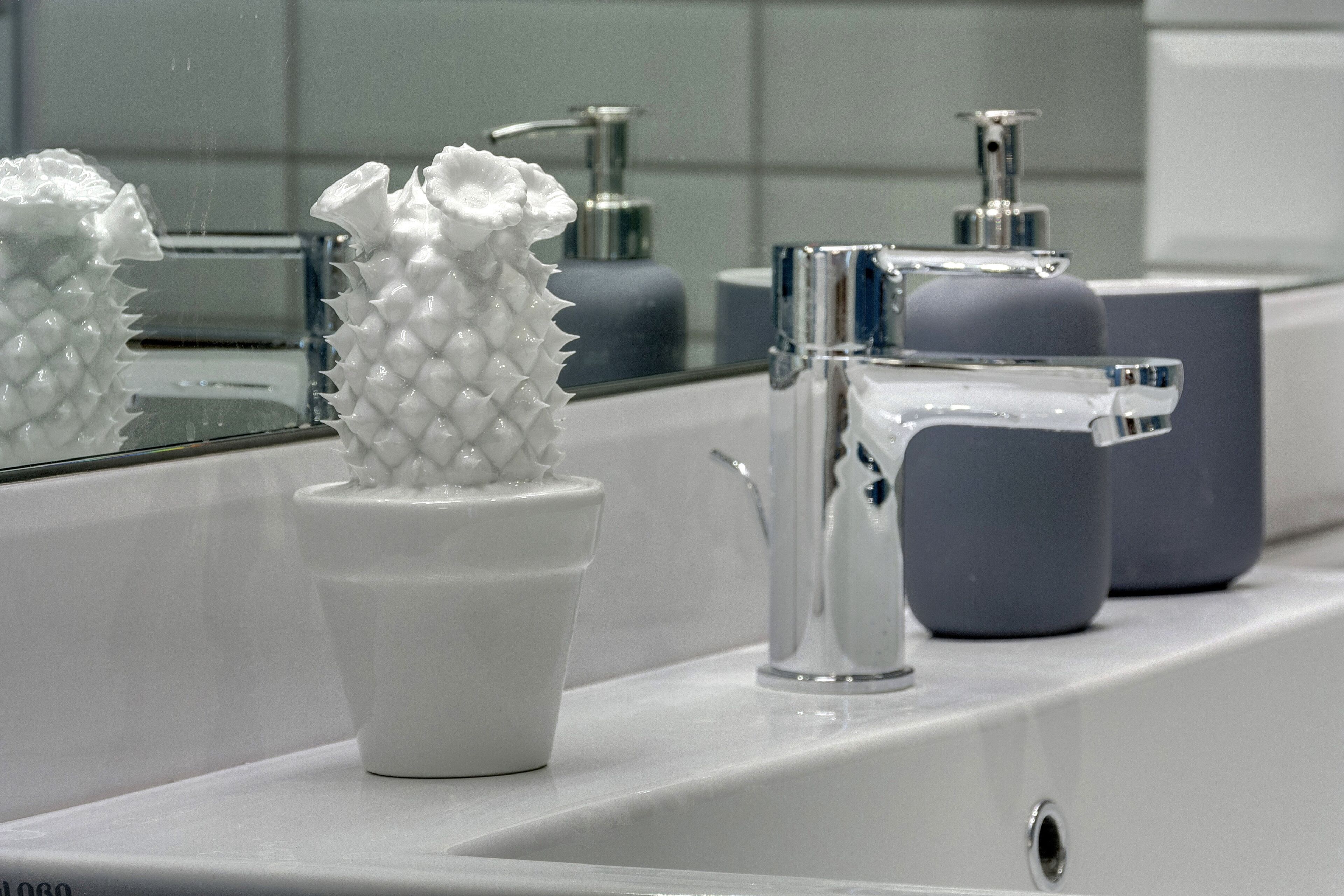 A bathroom with a white sink, a mirror, and a white cactus-shaped vase.