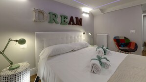 A neatly made bed with white linens, a green desk lamp, and a colorful chair. - Mamo Florence - St. Elizabeth Loft Apartment (Florence)