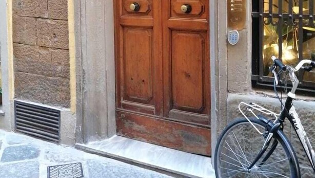 A wooden double door with a metal grille, a bicycle parked outside, and a stone-paved street. - Mamo Florence - St. Elizabeth Loft Apartment (Florence)