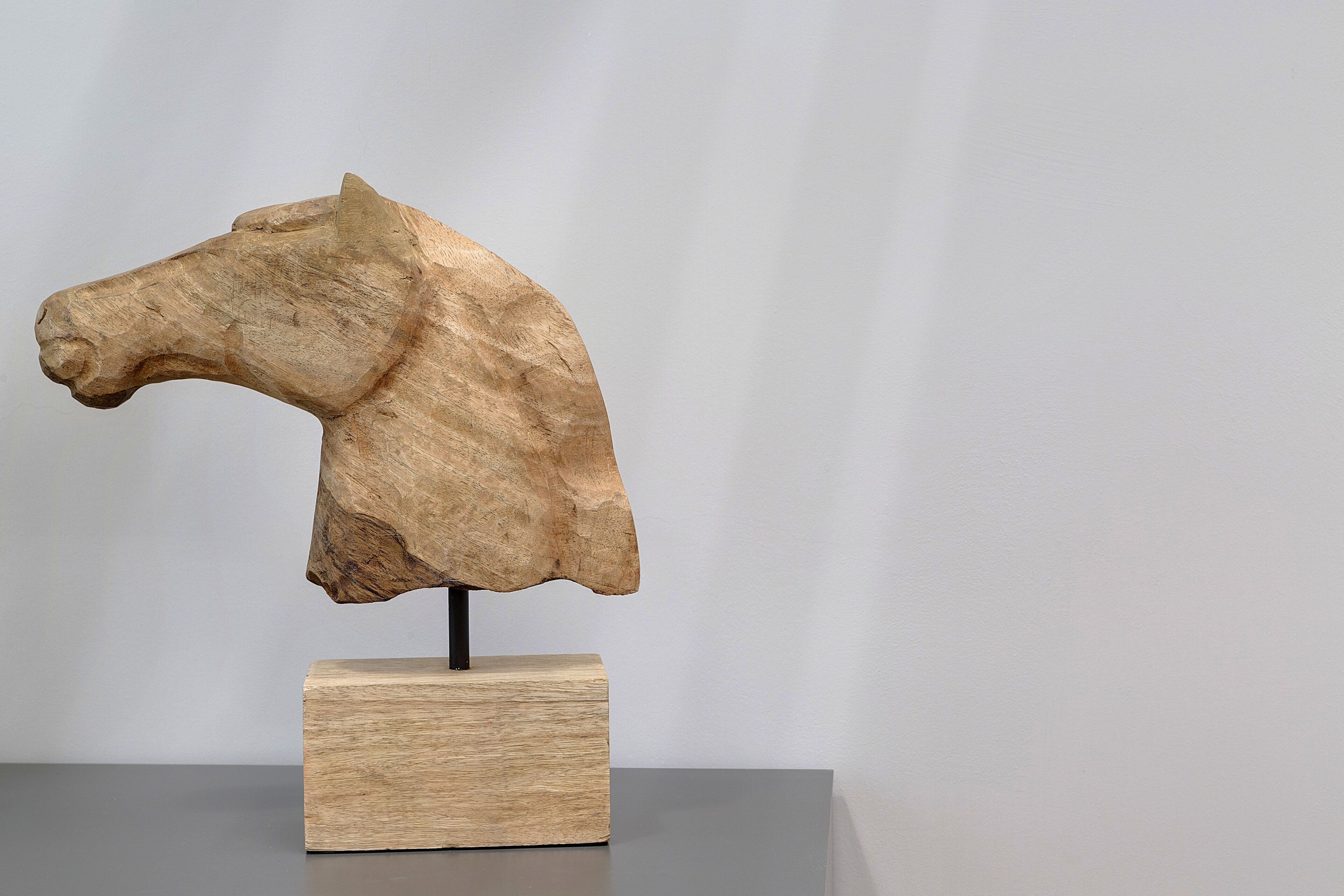 Une sculpture en bois représentant la tête d’un cheval, fixée sur un bloc.