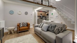 A modern living room with a grey sofa, wooden flooring, and a staircase. - Mamo Florence - St. Elizabeth Loft Apartment (Florence)