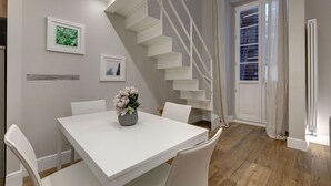 A dining area with a white table and chairs, a staircase, and a window with blinds. - Mamo Florence - St. Elizabeth Loft Apartment (Florence)