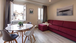 A modern living room with a red sofa, a dining table with chairs, and a large window with curtains. - Mamo Florence – Neri22 Apartments (Florence)