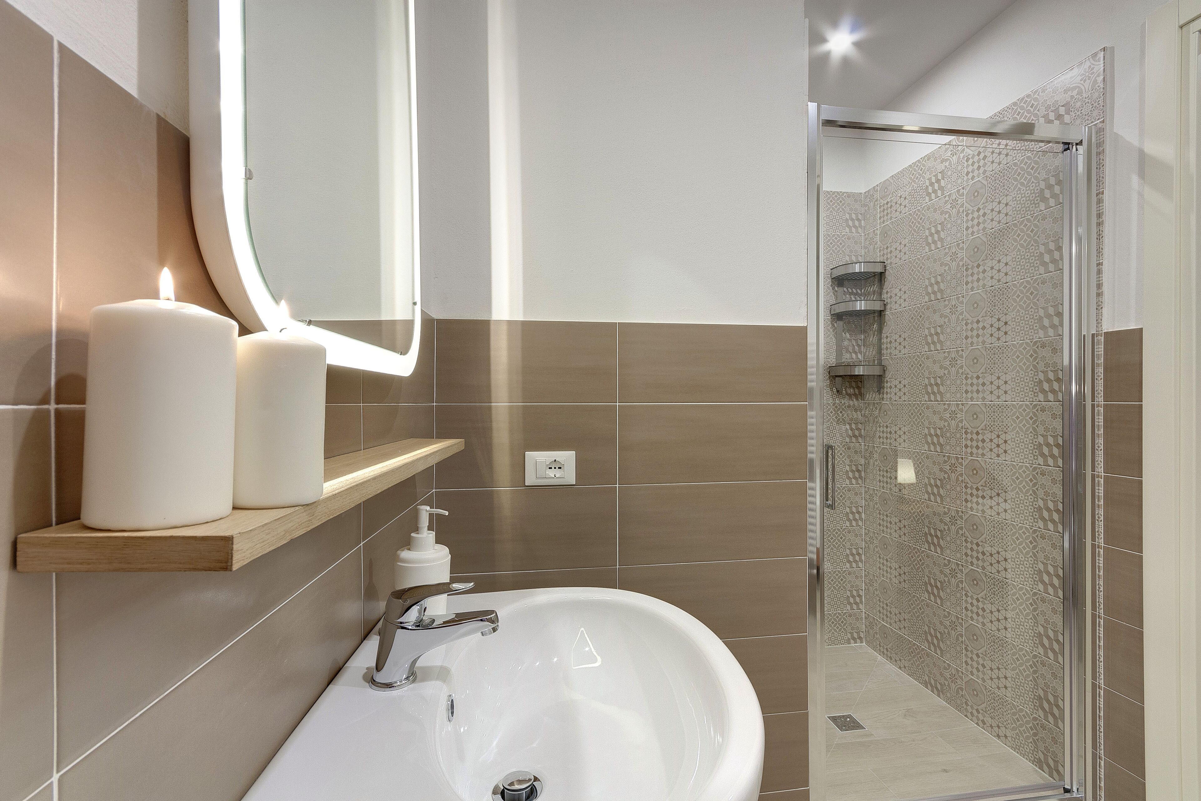 A bathroom with a white sink, two candles, a mirror, and a shower area with patterned tiles.