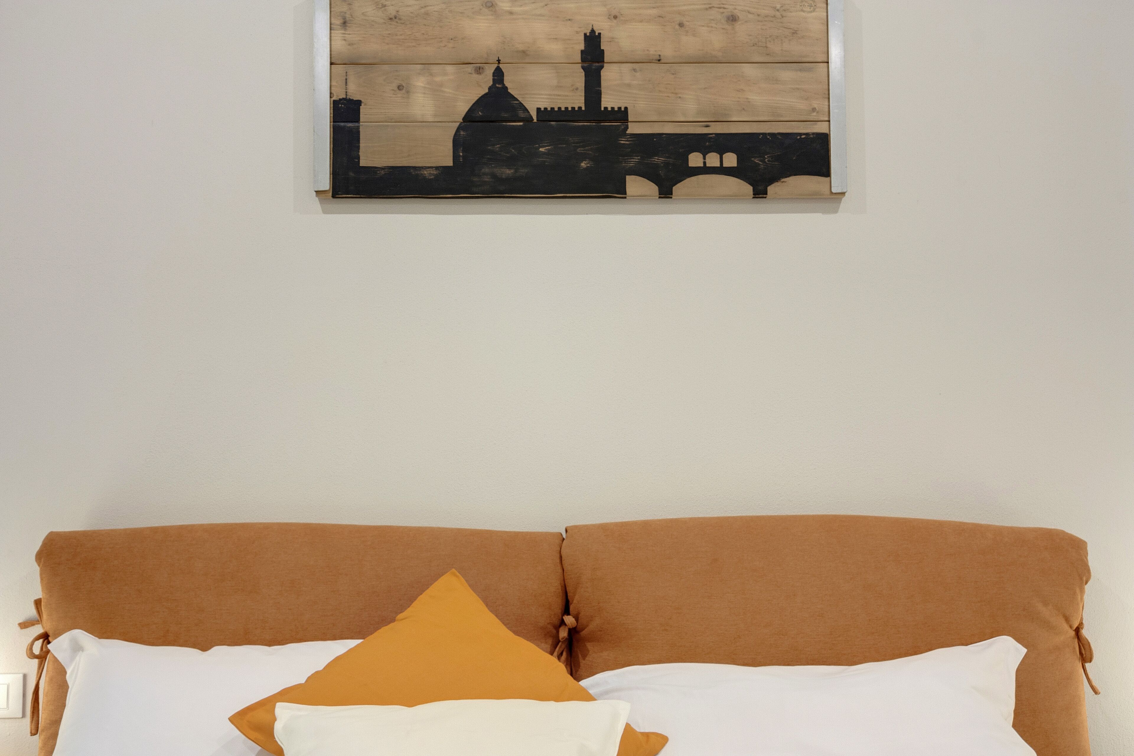 Una cama con cabecera marrón y almohadas blancas y mostaza.
