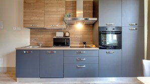 A modern kitchen with grey cabinets, a stainless steel range hood, a microwave, and an oven. - Mamo Florence – Neri22 Apartments (Florence)