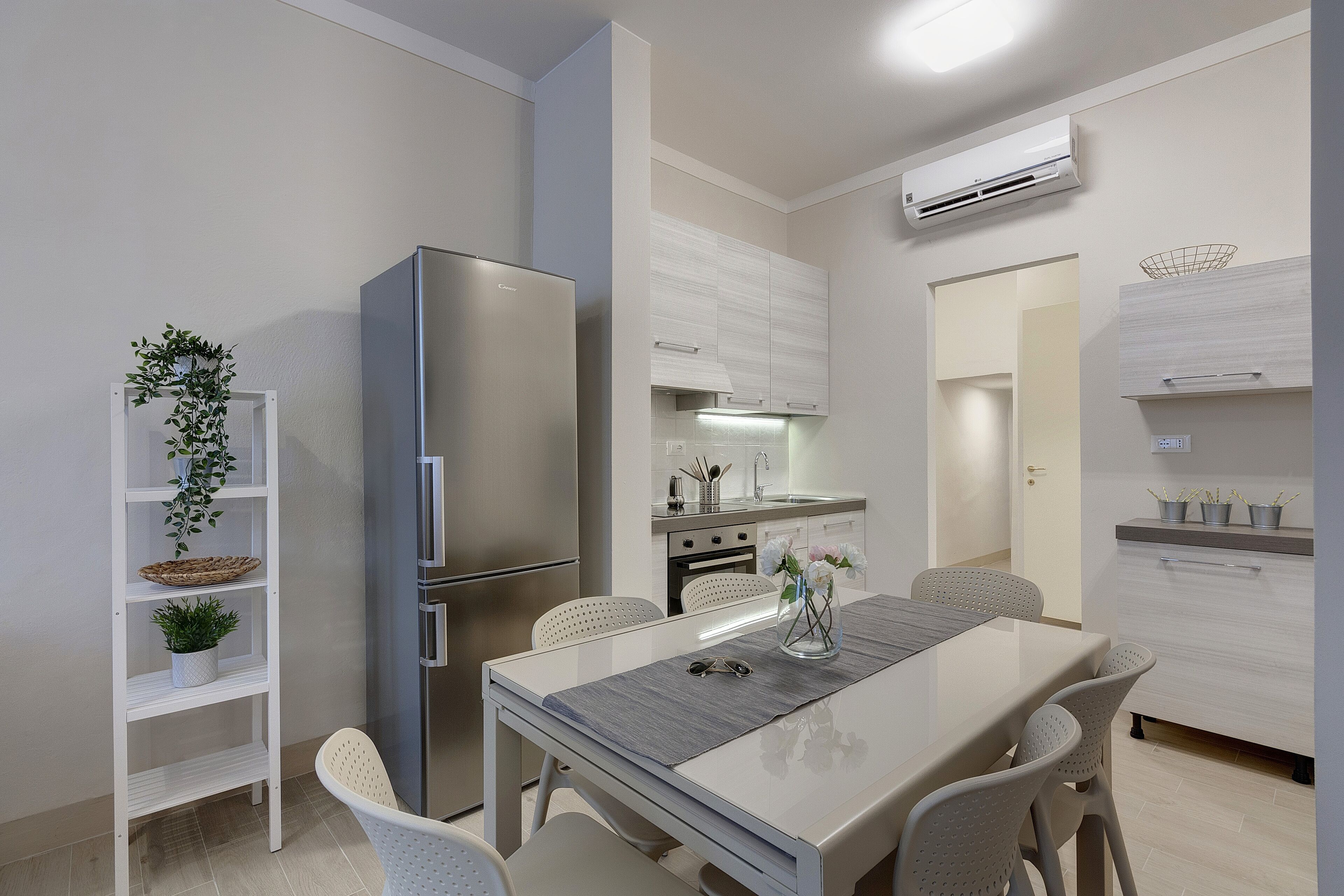 Una cocina moderna con armarios blancos, un refrigerador de acero inoxidable y un comedor con mesa y sillas.