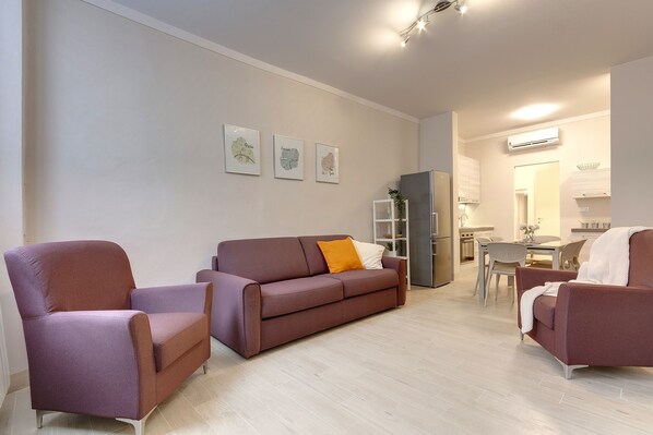 A modern living room with a sofa, armchairs, and a dining area. - Mamo Florence – Neri22 Apartments (Florence)