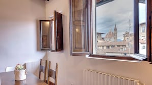 A dining area with a wooden table, chairs, a white radiator, and a window with a view of a historic building. - Mamo Florence – Neri22 Apartments (Florence)