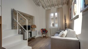 Un saló modern amb una escala, un sofà gris, una cadira colorida i una paret de pedra.