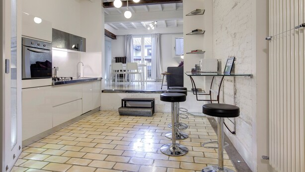 A modern kitchen with a built-in oven, a dining area with a table and chairs, and a bar area with stools. - Mamo Florence – Victor Apartment (Florence)
