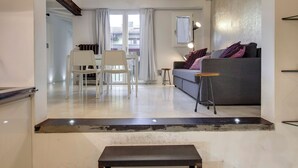 A modern living room with a grey sofa, a small table, and a white chair. There is a staircase leading to an upper floor. - Mamo Florence – Victor Apartment (Florence)