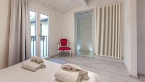 A hotel room with a bed, a red chair, a sliding glass door, and a radiator. - Mamo Florence – Victor Apartment (Florence)