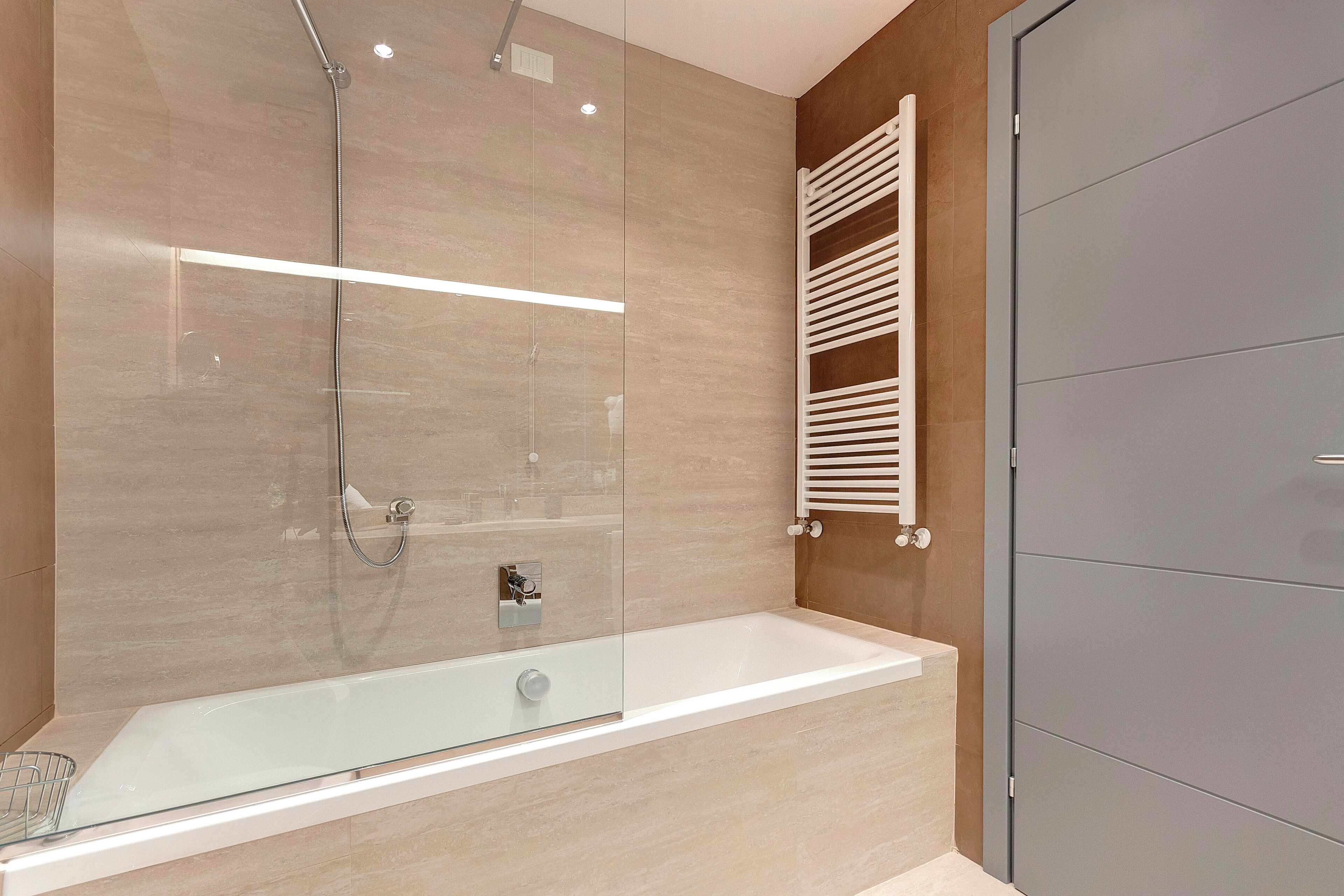 A modern bathroom with a glass-enclosed shower, a white bathtub, and a grey wardrobe.
