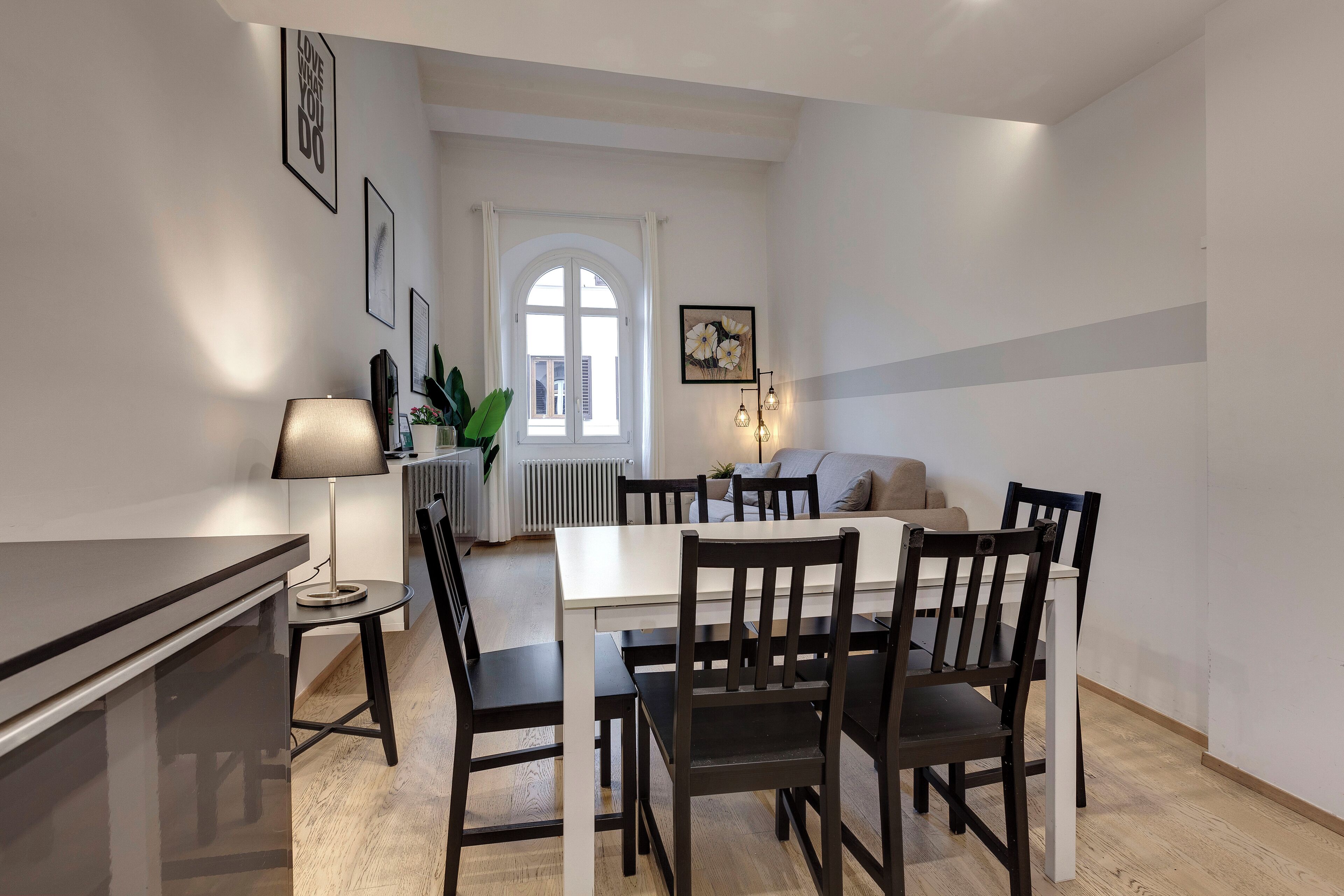 A modern dining area with a white table, black chairs, and a lamp.