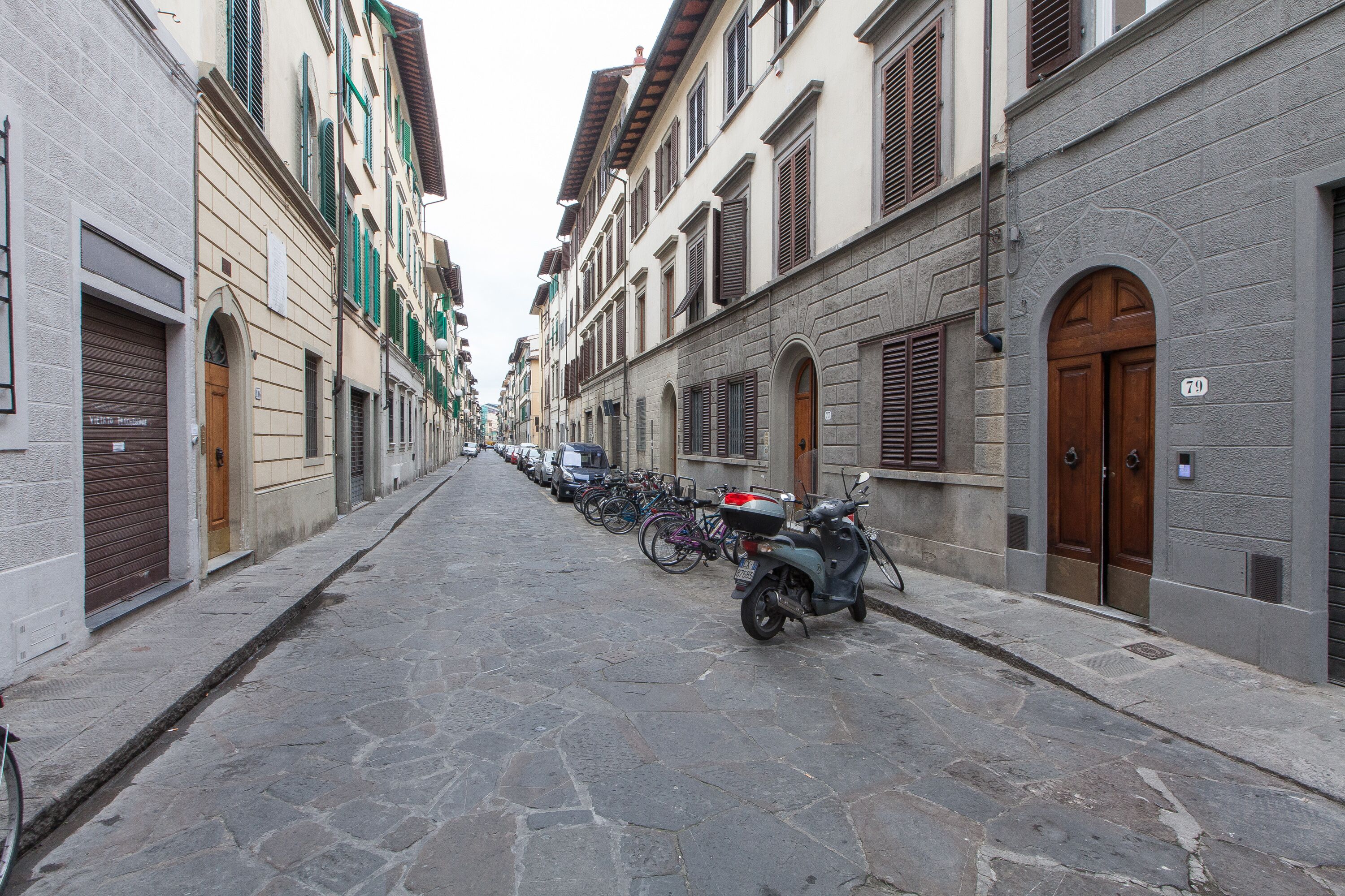 Een smalle straat met historische gebouwen, geparkeerde fietsen en een scooter.