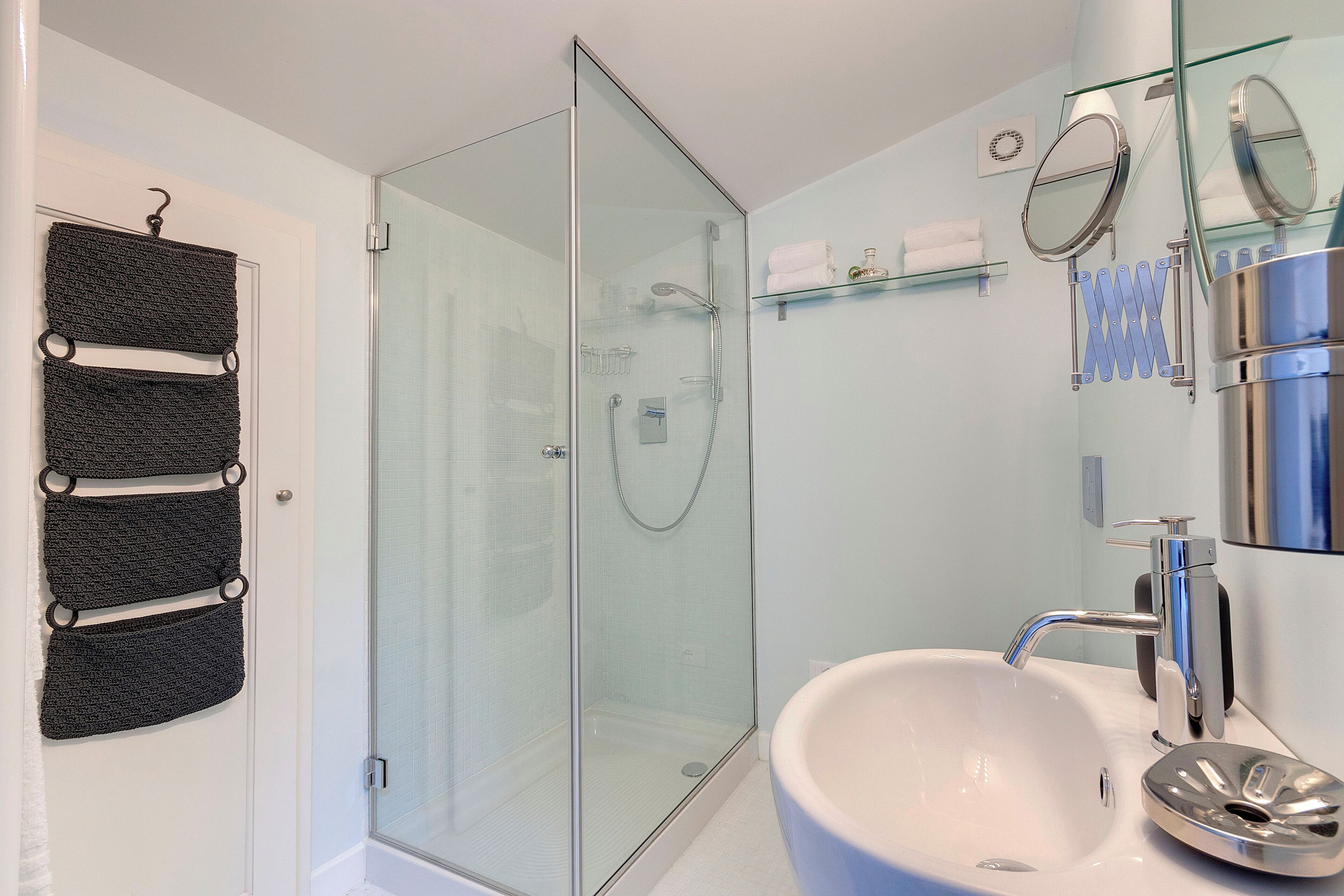 Un bagno moderno con doccia vetro, lavandino bianco con rubinetteria cromata e ripiano in vetro con articoli da toilette.