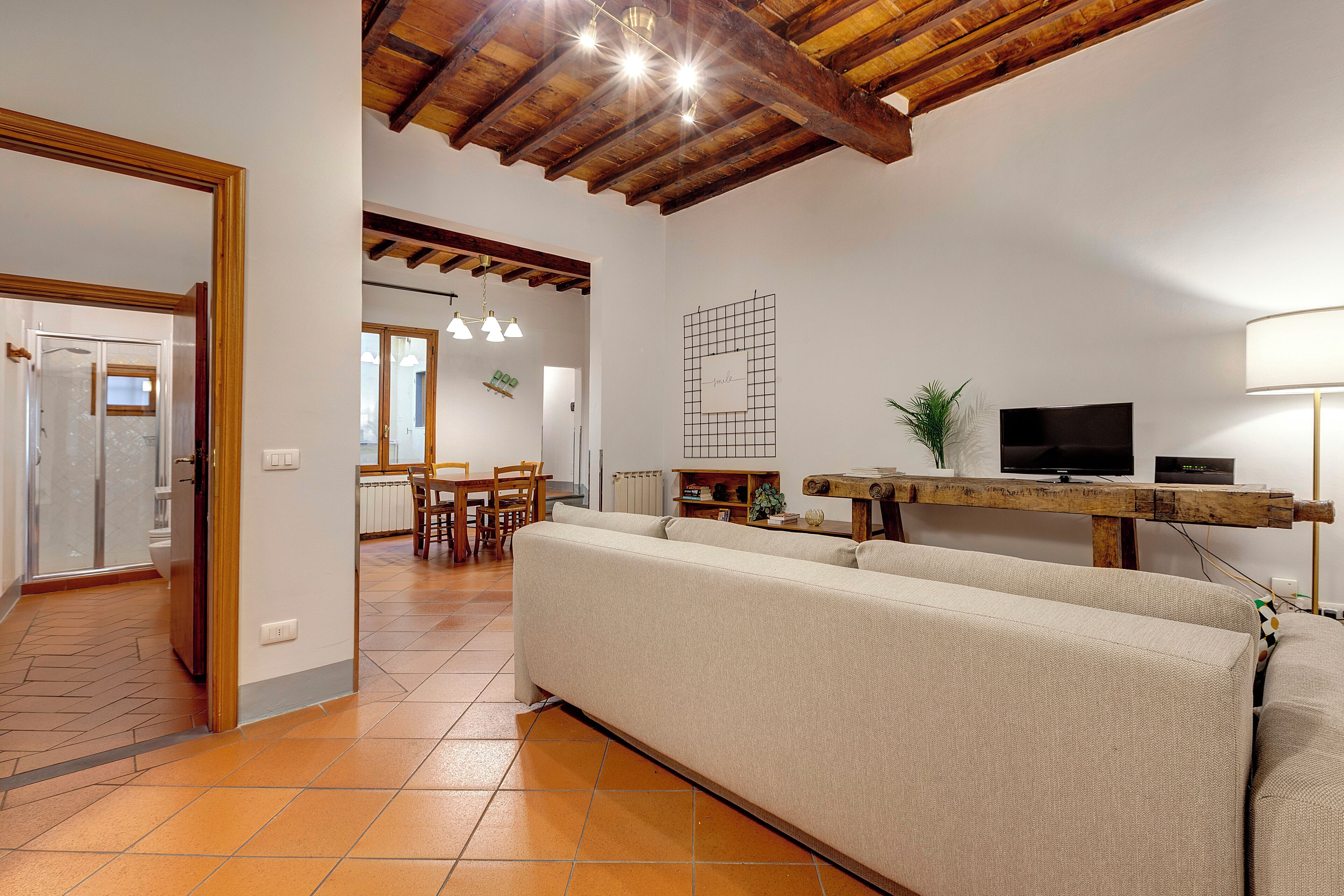 A living room with a sofa, wooden ceiling beams, a television, and a dining area with chairs and a table.