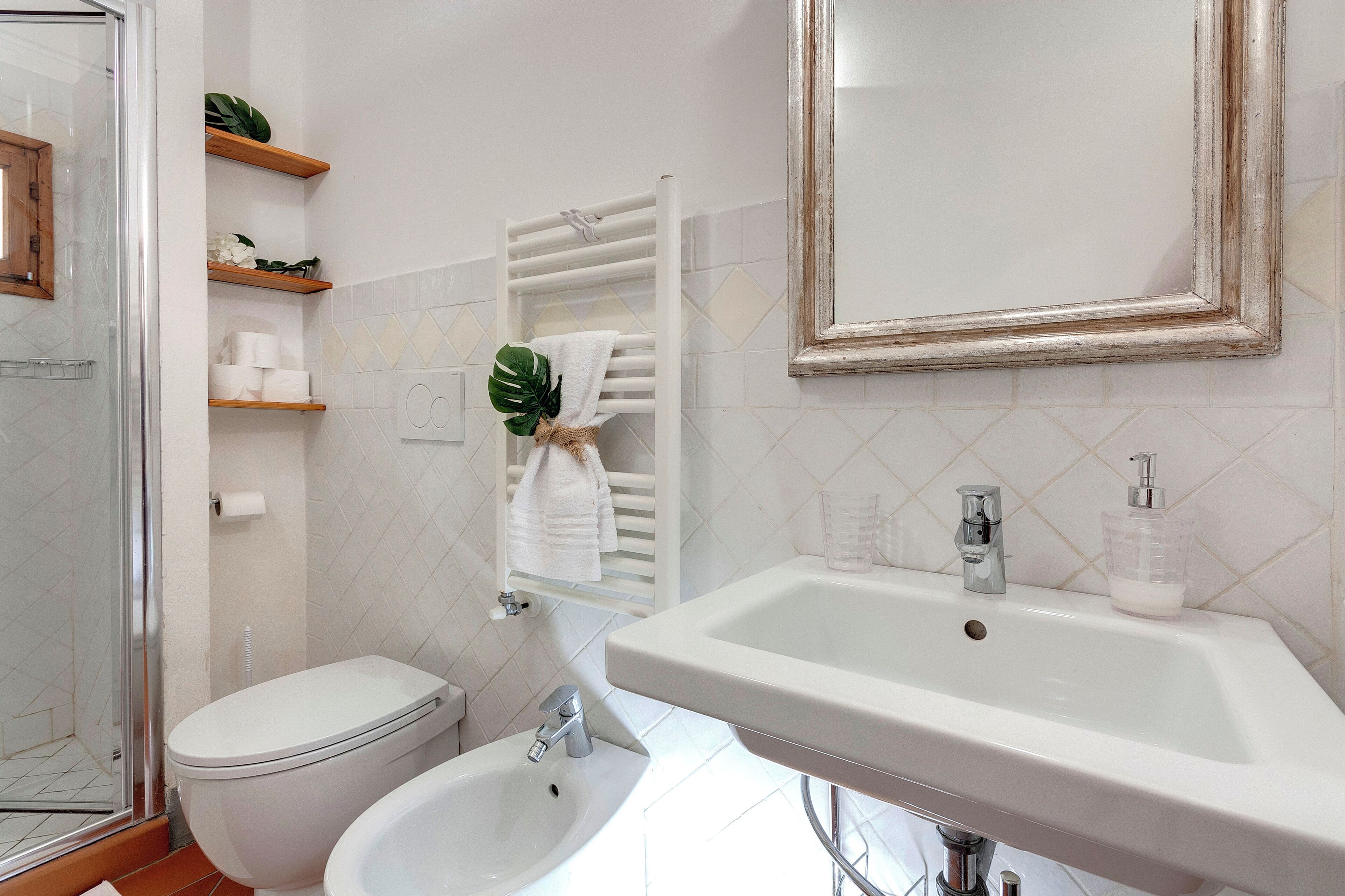 Un baño con inodoro, bidé, lavamanos y un perchero con toalla.