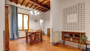 A dining area with a wooden table and chairs, a ceiling with exposed beams, a radiator, and a grid wall with a 'mile' sign. - Mamo Florence - Zeno Apartment (Florence)