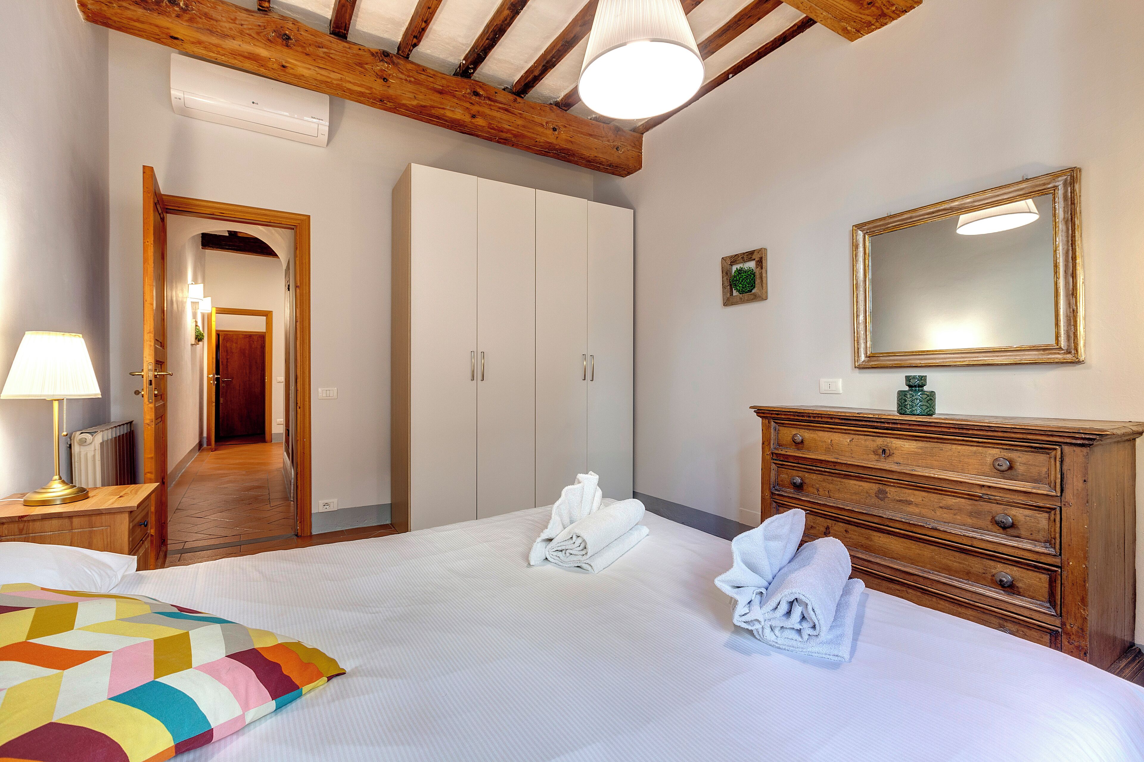 A bedroom with a bed, a dresser, a mirror, and a door leading to another room.