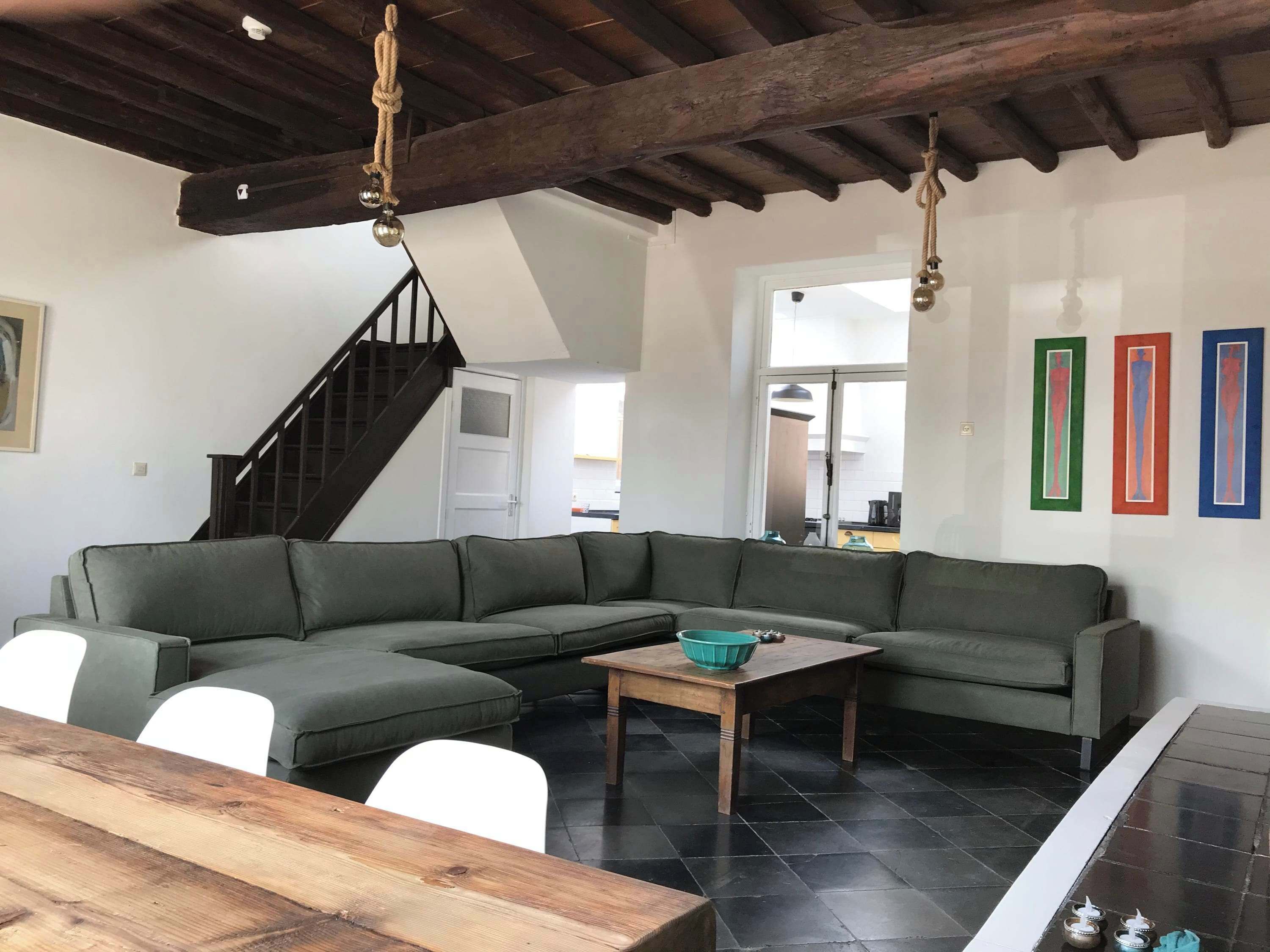 Una sala de estar con un sofá modular, una mesa de centro de madera, una escalera y vistas a la cocina.