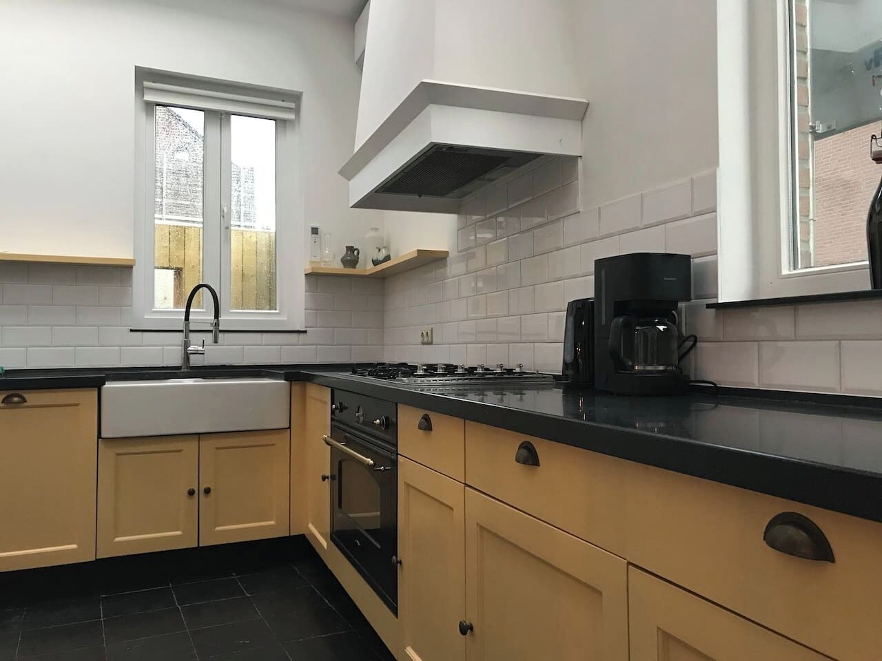 A kitchen with a black countertop, beige cabinets, a sink, a stove, and a coffee maker.