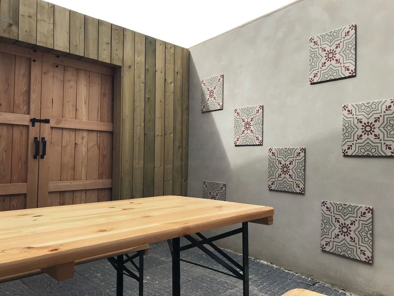 Une pièce avec une table en bois, un mur gris orné de carreaux décoratifs et une porte en bois.