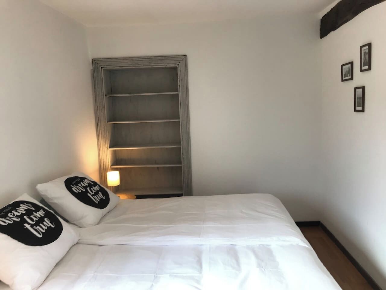 Een slaapkamer met een bed, kussens, een kledingkast en een wandplank.